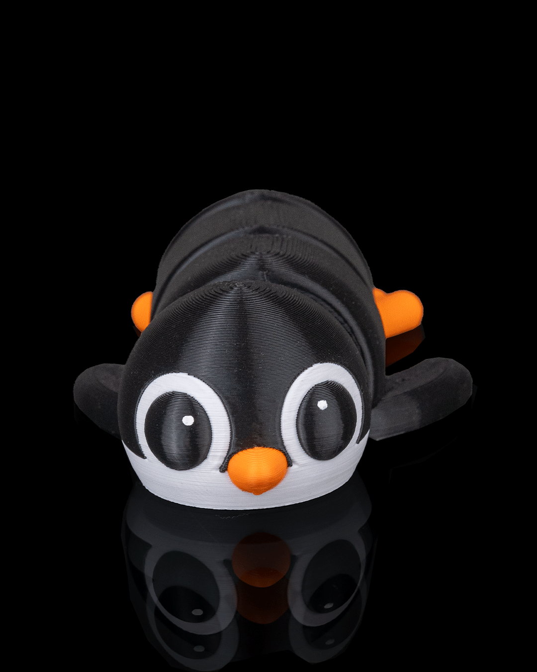 Flexi toy penguin with black body, white face, and orange beak and feet on a reflective black surface.